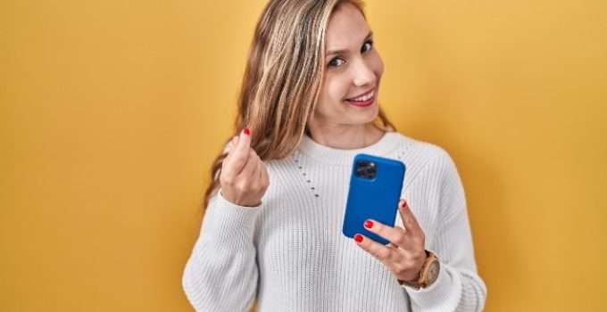 mujer sostiene móvil en una mano y en la otra mechón con reflejos