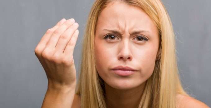 Jovencita de cabello decolorado con gesto de disgusto hace gesto de duda con la mano