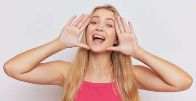 Una jovencita rubia sonríe y enmarca su cara con las manos