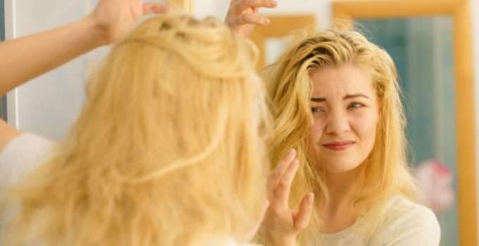 Una chica frente al espejo muy disgustada porque su pelo está amarillo