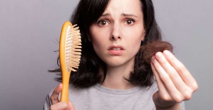 Una joven sostiene un cepillo y pelo en cada mano, preocupada porque se le cae el cabello