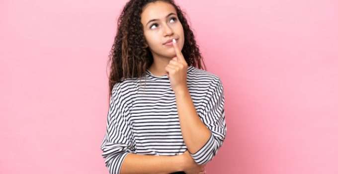 Una muchacha mira hacia arriba con gesto de duda porque no sabe si hacerse primero el alisado o el tinte