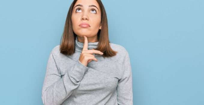 Una chica con dudas con su dedo en la barbilla mirando hacia el cielo