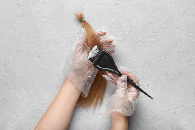Unas manos con guante aplican mezcla de tintes sobre un mechón de cabello para experimentar 
