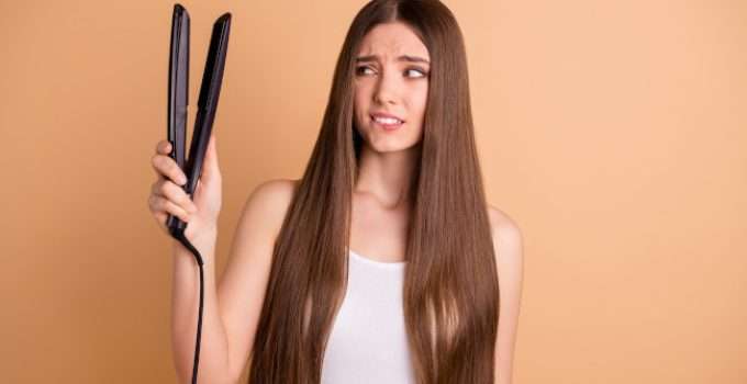Jovencita mira con dudas su plancha de cabello porque no sabe cuántas veces debe pasarla para la keratina